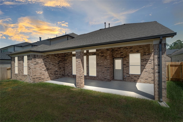 back house at dusk featuring a lawn and a patio area