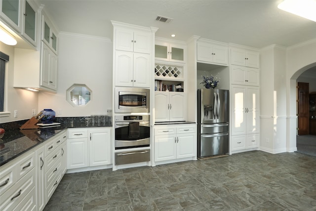 kitchen with stainless steel appliances, dark stone counters, white cabinetry, and ornamental molding