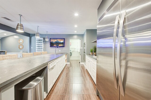 kitchen featuring pendant lighting, light tile patterned floors, appliances with stainless steel finishes, sink, and white cabinets