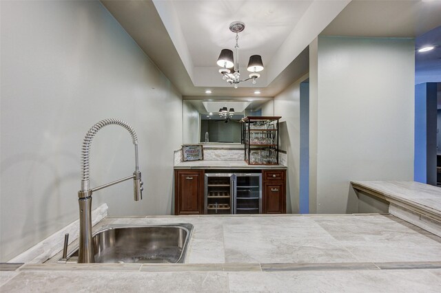 kitchen with hanging light fixtures, a chandelier, sink, a raised ceiling, and beverage cooler