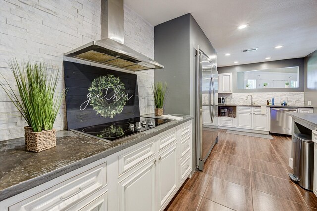 kitchen featuring white cabinets, tile patterned floors, appliances with stainless steel finishes, wall chimney exhaust hood, and decorative backsplash