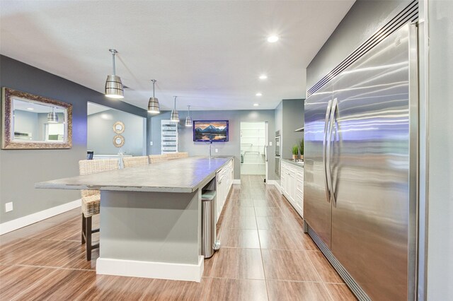 kitchen with white cabinets, stainless steel built in fridge, a center island, light tile patterned flooring, and a breakfast bar