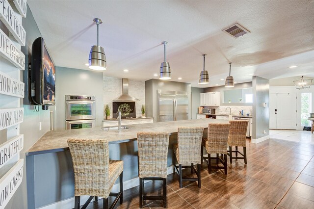 kitchen with dark tile patterned flooring, stainless steel appliances, a kitchen breakfast bar, wall chimney exhaust hood, and white cabinets