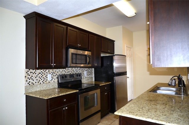 kitchen with tasteful backsplash, light tile patterned floors, light stone counters, sink, and appliances with stainless steel finishes