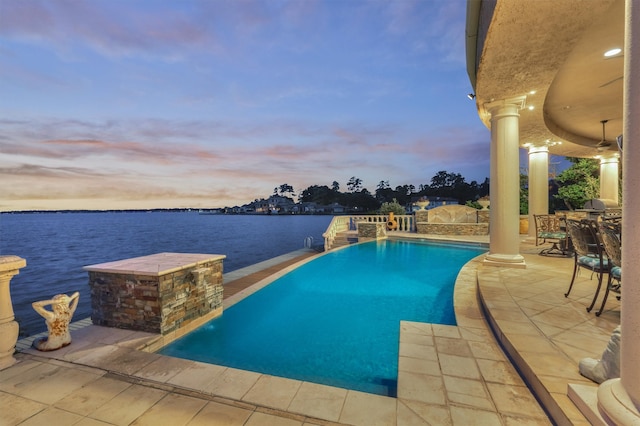 pool at dusk featuring a patio area, pool water feature, and a water view