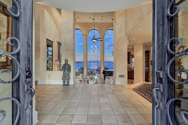 entrance foyer with a towering ceiling, a water view, ceiling fan, and tile patterned flooring