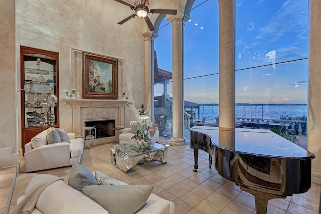 living room featuring light tile patterned floors, a water view, a premium fireplace, ceiling fan, and a towering ceiling