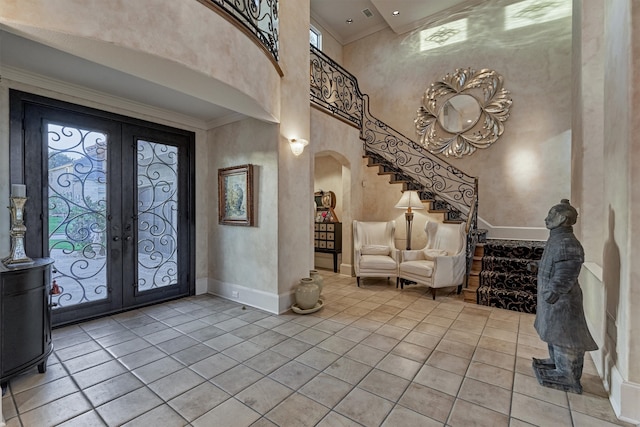 entryway with a high ceiling, light tile patterned floors, crown molding, and french doors