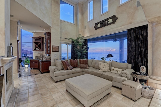 tiled living room featuring a towering ceiling, a water view, ceiling fan, and a healthy amount of sunlight