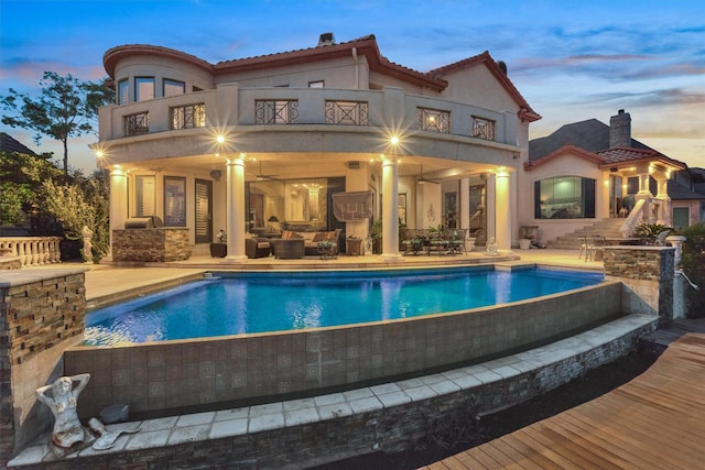 rear view of house featuring a patio, a balcony, stucco siding, an outdoor hangout area, and an infinity pool