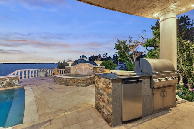 patio terrace at dusk featuring area for grilling, a grill, and a water view