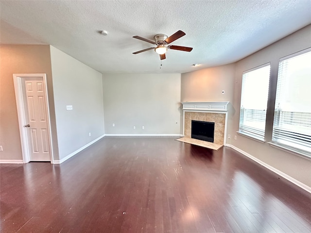 unfurnished living room featuring ceiling fan, a tile fireplace, dark hardwood / wood-style flooring, and a textured ceiling