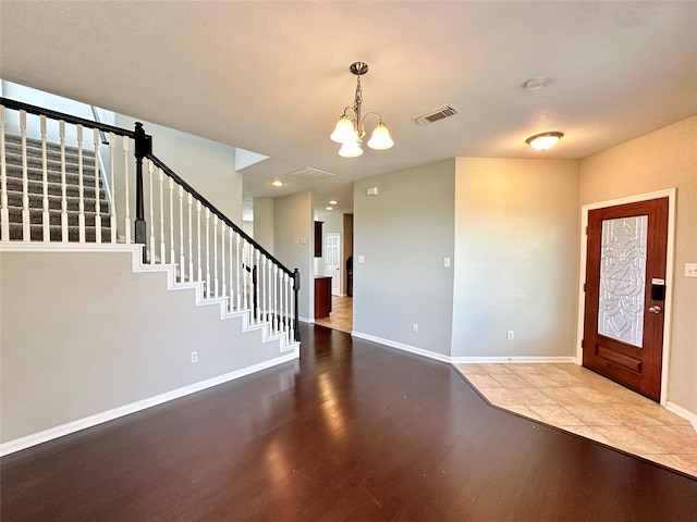 entrance foyer featuring visible vents, wood finished floors, stairway, an inviting chandelier, and baseboards