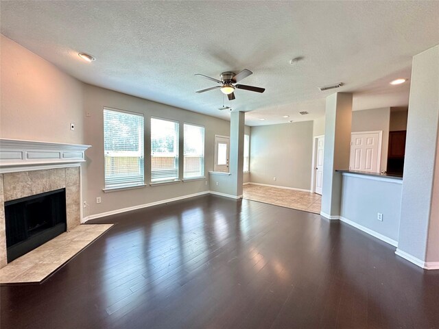 unfurnished living room with dark wood-type flooring, ceiling fan, a tiled fireplace, and a textured ceiling