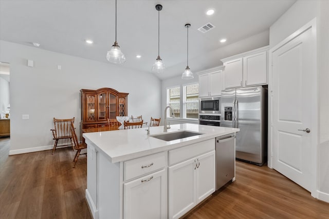 kitchen featuring a center island with sink, pendant lighting, stainless steel appliances, sink, and white cabinets