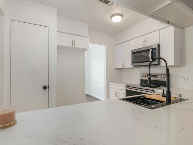 kitchen featuring white cabinets, appliances with stainless steel finishes, backsplash, and light stone countertops