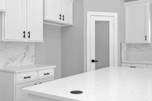 kitchen featuring light stone countertops, backsplash, and white cabinets