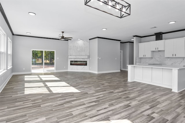 unfurnished living room with ceiling fan, ornamental molding, light wood-type flooring, and a fireplace