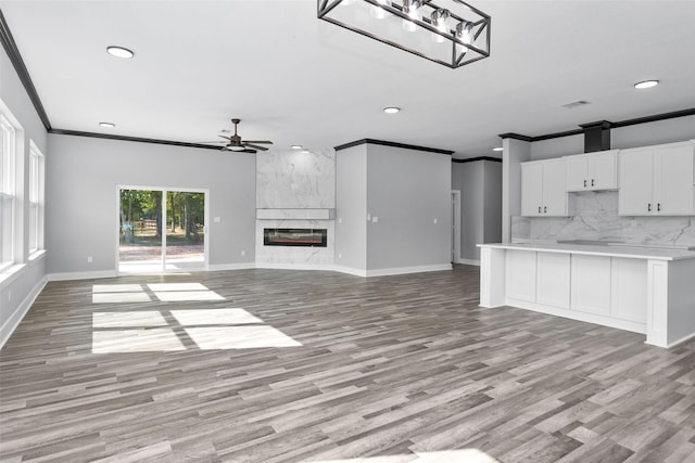 unfurnished living room with light wood finished floors, a premium fireplace, ornamental molding, ceiling fan, and baseboards