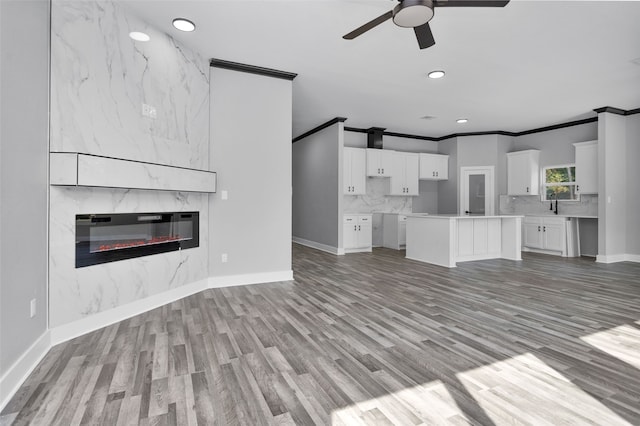 unfurnished living room with light wood-type flooring, crown molding, a premium fireplace, sink, and ceiling fan