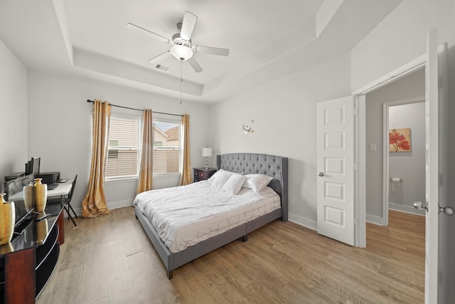 bedroom with ceiling fan, a raised ceiling, and light hardwood / wood-style flooring