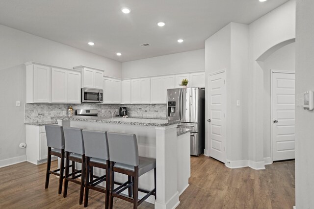 kitchen featuring hardwood / wood-style floors, appliances with stainless steel finishes, backsplash, and a breakfast bar area