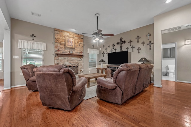 living room with light hardwood / wood-style flooring, ceiling fan, and a stone fireplace