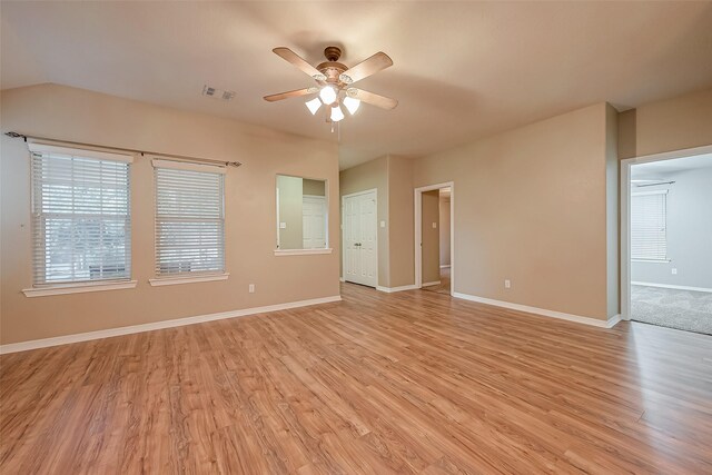 spare room featuring light wood finished floors, baseboards, visible vents, a ceiling fan, and vaulted ceiling