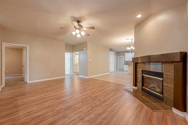 unfurnished living room with light wood finished floors, a fireplace, baseboards, and ceiling fan with notable chandelier