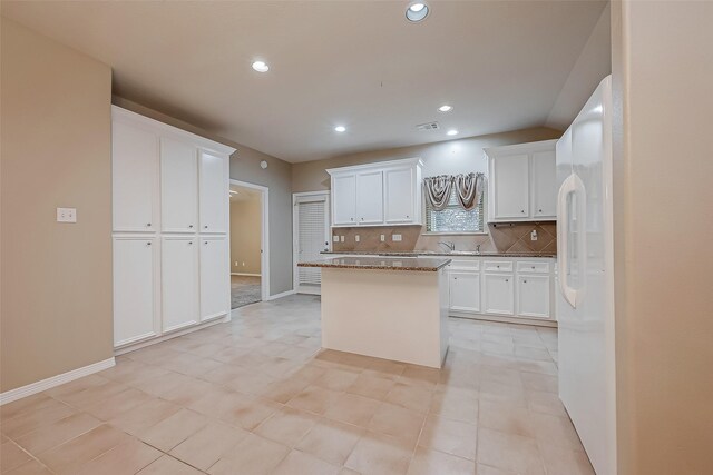 kitchen featuring freestanding refrigerator, white cabinets, a kitchen island, and backsplash