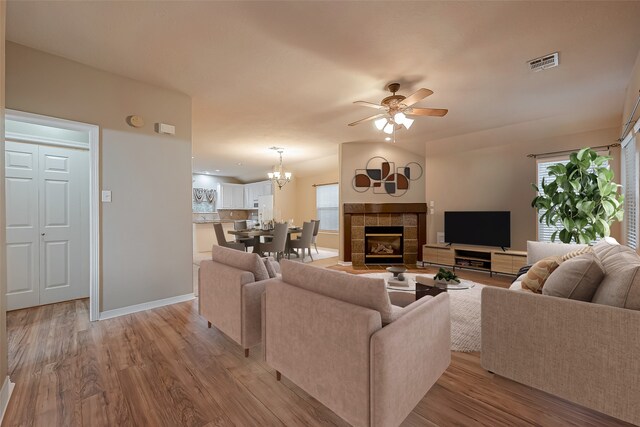 living room with light wood finished floors, visible vents, a tiled fireplace, baseboards, and ceiling fan with notable chandelier