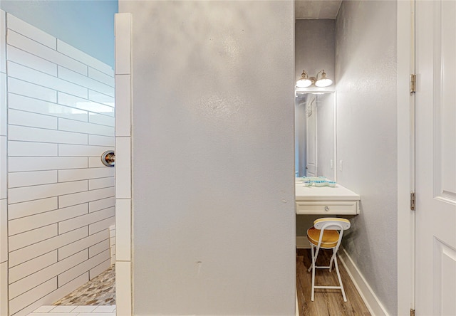 bathroom with a tile shower and wood-type flooring