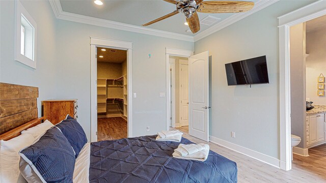 bedroom featuring ceiling fan, light hardwood / wood-style flooring, ensuite bath, a spacious closet, and crown molding