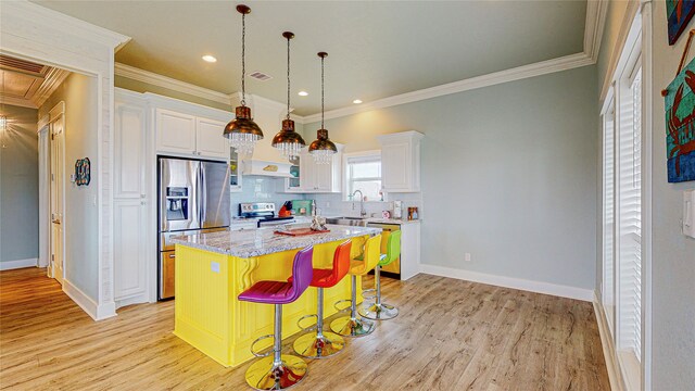 kitchen with light hardwood / wood-style floors, white cabinets, stainless steel appliances, a kitchen bar, and a center island