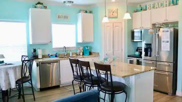 kitchen with light hardwood / wood-style flooring, decorative light fixtures, appliances with stainless steel finishes, light stone countertops, and a kitchen island