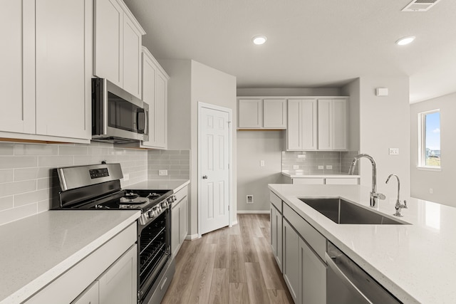 kitchen with light stone counters, a sink, white cabinets, light wood-style floors, and appliances with stainless steel finishes