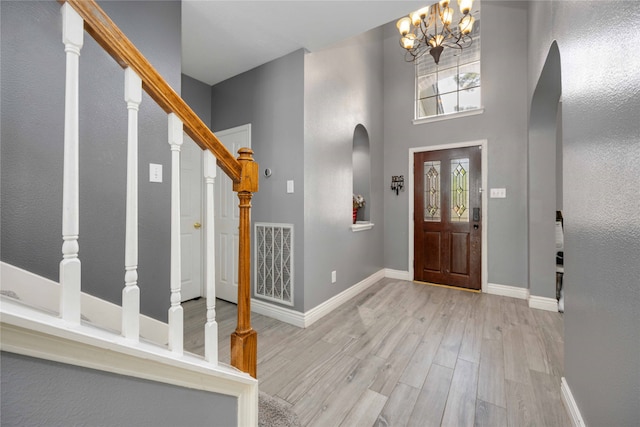 foyer entrance with a towering ceiling, light hardwood / wood-style flooring, and a notable chandelier