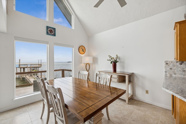 tiled dining area with high vaulted ceiling, a water view, ceiling fan, and a textured ceiling