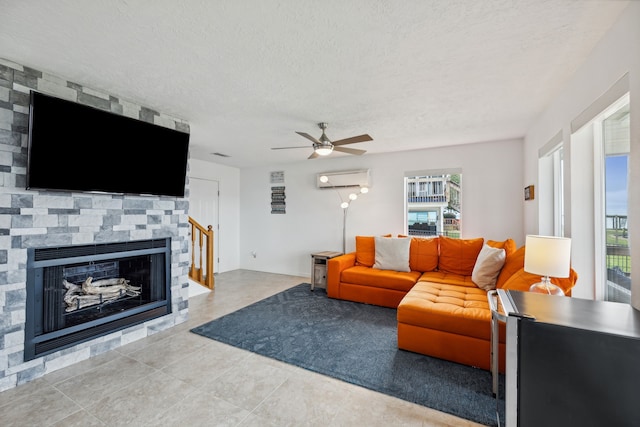 living room with a wealth of natural light, a wall mounted AC, ceiling fan, and a stone fireplace