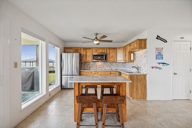 kitchen featuring stainless steel appliances, a kitchen island, sink, ceiling fan, and decorative backsplash