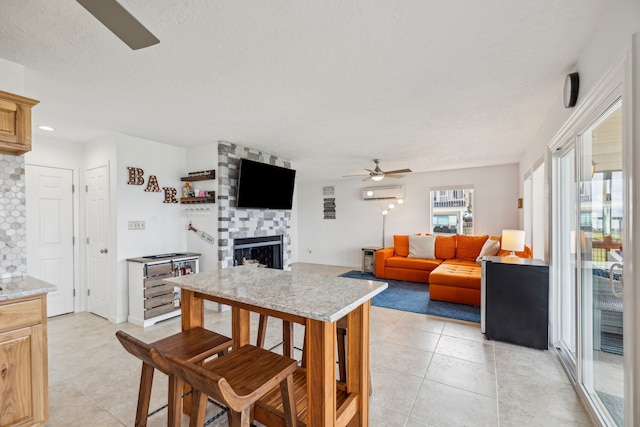 tiled dining room featuring ceiling fan, a textured ceiling, an AC wall unit, and a stone fireplace