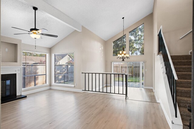 unfurnished living room with beam ceiling, a textured ceiling, ceiling fan with notable chandelier, light hardwood / wood-style flooring, and a tile fireplace