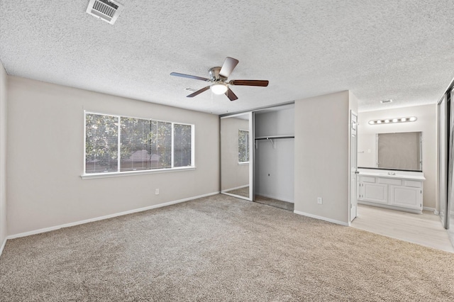 unfurnished bedroom with ceiling fan, a closet, light carpet, and connected bathroom