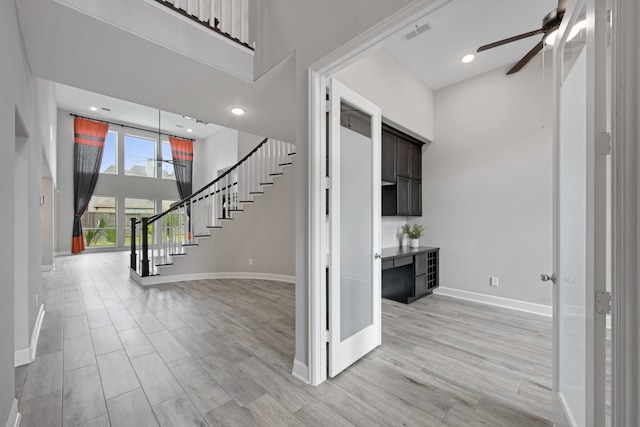 entrance foyer with ceiling fan, a towering ceiling, and light wood-type flooring