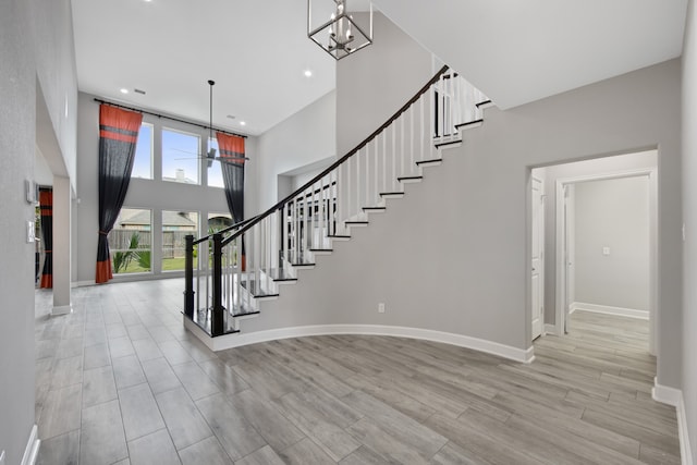 stairway with a towering ceiling, a notable chandelier, and hardwood / wood-style flooring