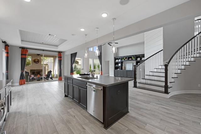 kitchen featuring a center island with sink, sink, hanging light fixtures, stainless steel dishwasher, and a tray ceiling