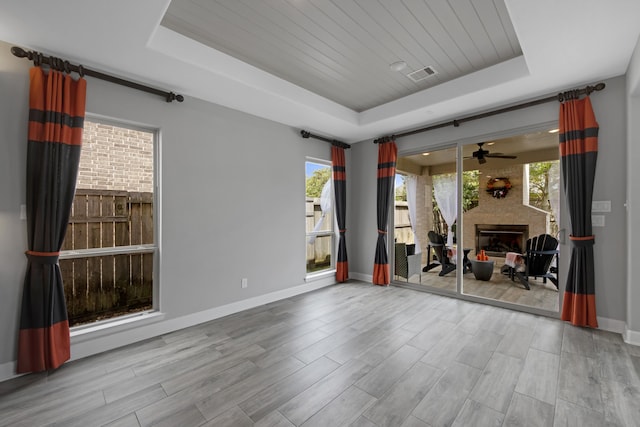 spare room featuring a raised ceiling, a fireplace, and light hardwood / wood-style flooring