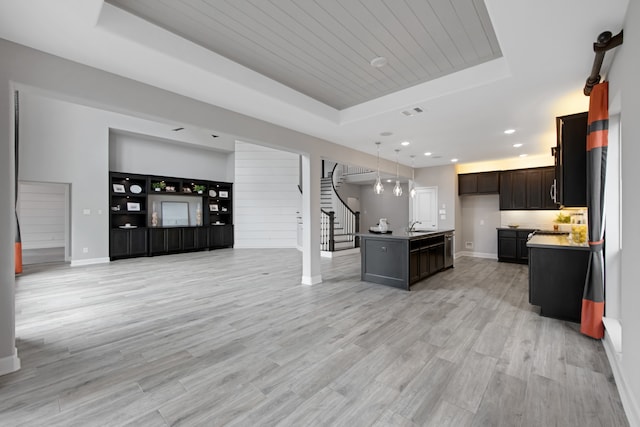 kitchen with pendant lighting, a kitchen island with sink, a raised ceiling, sink, and light hardwood / wood-style floors