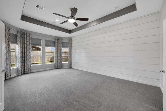 empty room featuring carpet floors, a tray ceiling, and ceiling fan