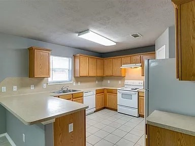 kitchen featuring white appliances, kitchen peninsula, sink, and light tile patterned flooring